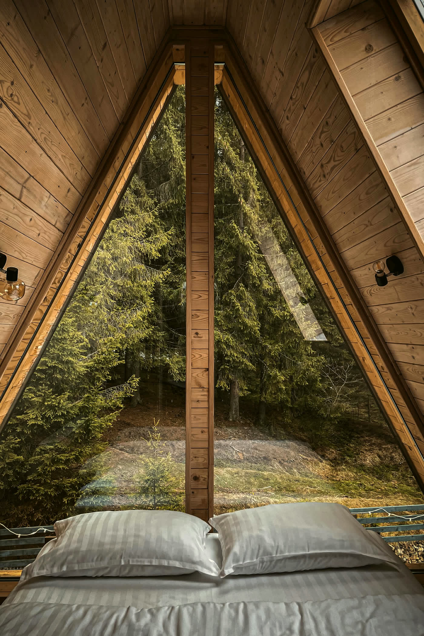 Bed under the triangular window of an A-frame cabin